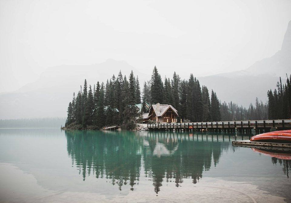Wooden buildings beside a still lake and forest